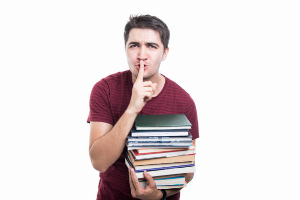 istock Student holding pile of books making sush gesture 854989692