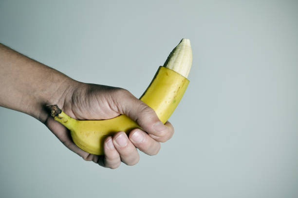 man with a banana with the tip of its skin removed closeup of the hand of a young man with a banana with the tip of its skin removed, depicting a circumcised male member penis photos stock pictures, royalty-free photos & images