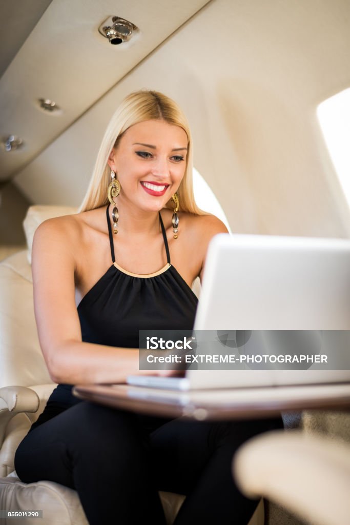 Woman in private jet airplane Blonde woman sitting inside private jet airplane and working on laptop computer. Adult Stock Photo