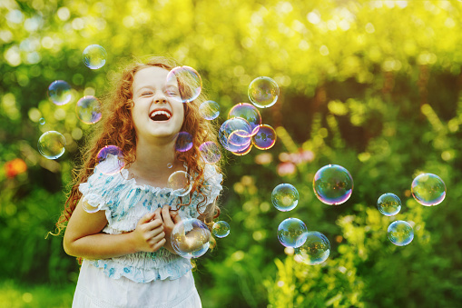 Laughing curly girl with bubbles.  Happy childhood concept.