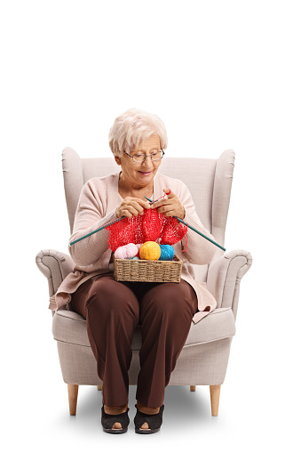 Elderly woman sitting in an armchair and knitting isolated on white background