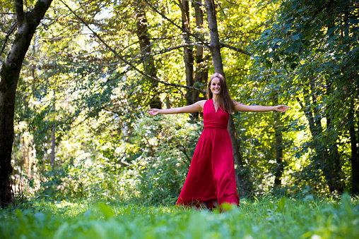 Beautiful young woman in red dress walking in nature.