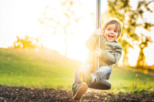 happy laughing little boy on zipline in bright sunshine cute three year old boy in warm clothes laughing and having fun on zipline in outdoor park autumn only boys stock pictures, royalty-free photos & images