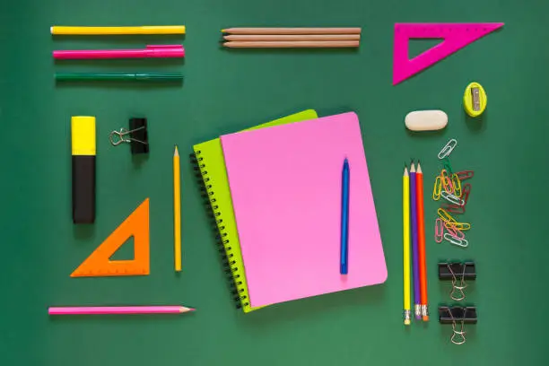 Photo of Colorful school supplies, pink book on green. Top view, flat lay, copy space.