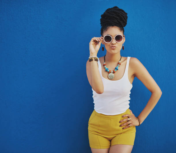 This summer, just call me Miss Cool Studio shot of an attractive young woman wearing funky sunglasses and pouting against a blue background black woman hair bun stock pictures, royalty-free photos & images