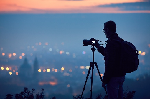 Silhouette of the photographer with tripod. Young man taking photo with his camera in the night city. Prague, Czech Republic.