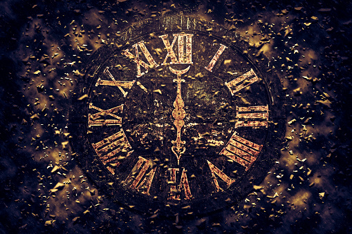 Closeup of an old clock dial with roman numbers in golden color, exploding in pieces