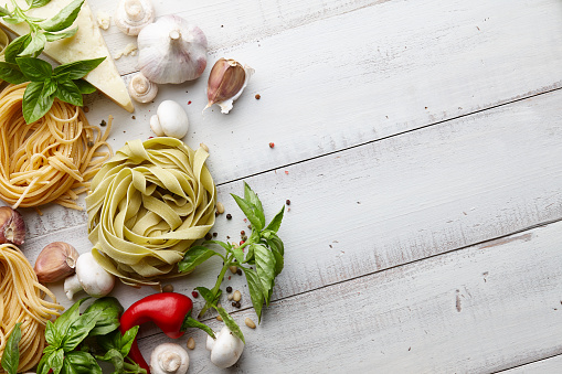 Raw homemade italian pasta and ingredients on white wooden background, cooking process