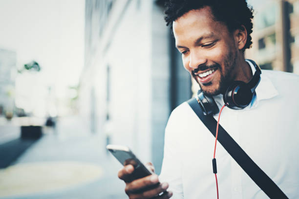 istock Young Smiling African man using smartphone on hands while standing at sunny city street.Concept of happy business people working outside.Blurred background. 855102224