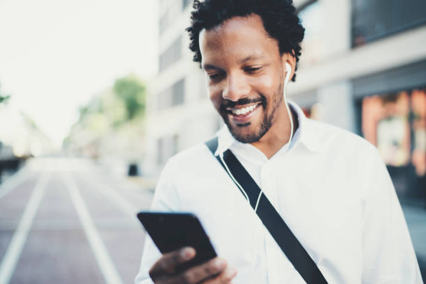istock Portrait of young smiling african man using smartphone hands while standing at sunny city street.Concept of happy business people working outside.Blurred background. 855102394