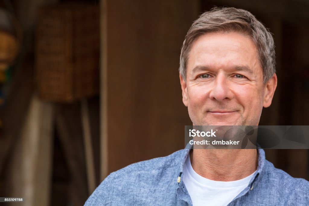 Mâle de beau, accomplis et heureux homme âgé moyen vêtu d’une chemise bleue, s’appuyant sur un poteau par un garage ou une grange - Photo de Hommes libre de droits