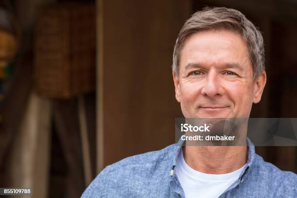 Uomo Di Mezza Età Bello Di Successo E Felice Che Indossa Una Camicia Blu Appoggiata Su Un Palo Da Un Garage O Un Fienile - Fotografie stock e altre immagini di Uomini