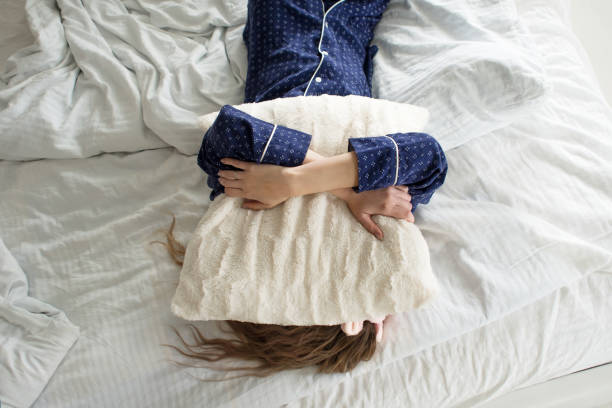 Too lazy to get out of bed, a woman covers her face with a pillow stock photo
