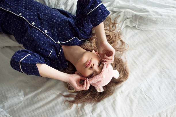 linda rubia en su cama en pijama azul y antifaz para dormir, vista superior - máscara para los ojos fotografías e imágenes de stock