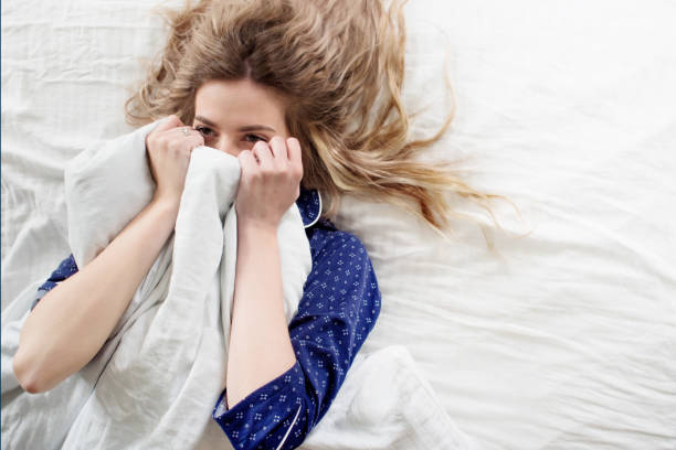 istock Cute blonde in her bed in blue pajamas, under a blanket 855117648