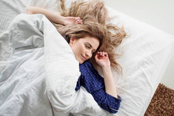 istock Cute blonde in her bed in blue pajamas, under a blanket 855117682