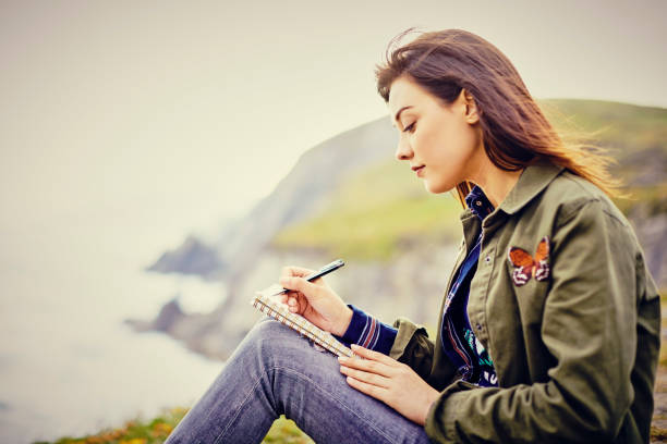istock Beautiful young woman writing in diary while sitting on mountain 855120740