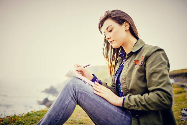 istock Beautiful woman writing in diary on mountain against clear sky 855120802