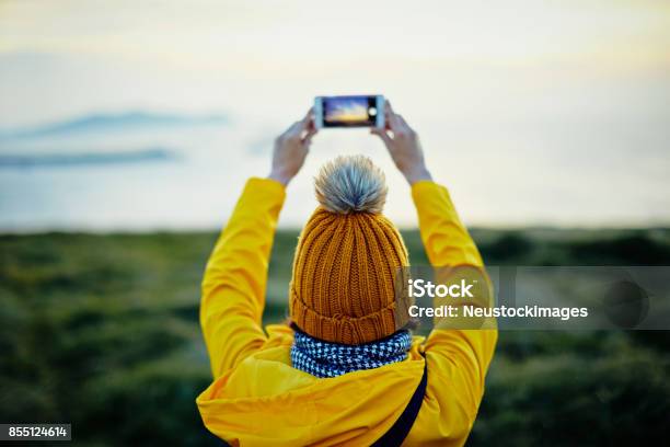 海に山にスマート フォンで撮影の女性観光客の後姿 - アイルランドのストックフォトや画像を多数ご用意 - アイルランド, 写真メール, 黄色