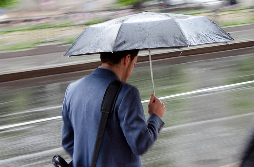 Belgrade: Man in a suit walking in a  under umbrella on a rainy day in the city street, panning shot