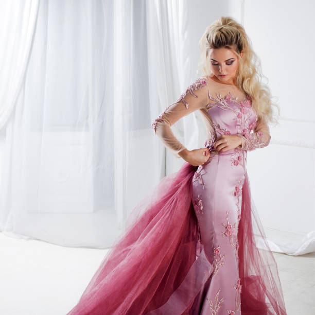 istock Glamorous lady in a chic pink dress with a train. Studio portrait in white interior 855131334