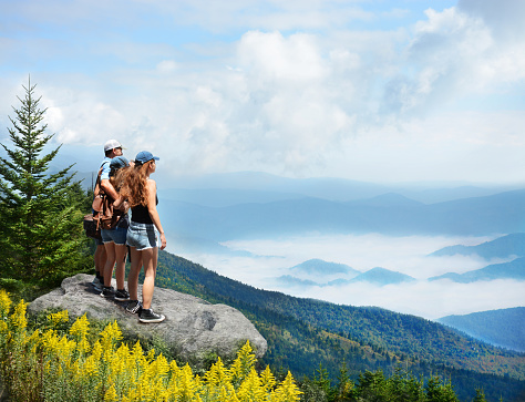 Family hiking on vacation. Father standing with arms around his family on top of mountain, over clouds, looking at beautiful foggy landscape.Near Asheville, Blue Ridge Mountains, North Carolina, USA.