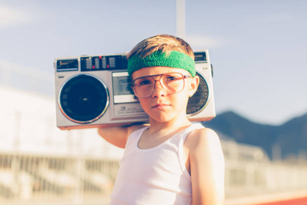 Young Retro Fitness Boy Listening to Music A young boy dressed in headband and retro workout attire is having a great time listening to music on his boombox. He has a serious expression on his face and is excited for health. stereo photos stock pictures, royalty-free photos & images