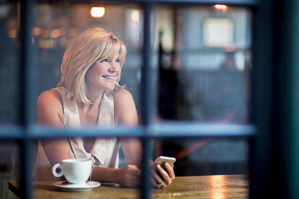istock Mature woman reading a message on her mobile phone while having a coffee in a pub 855143038