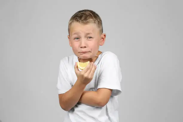 Little, blond boy biting into a lemon and make a face