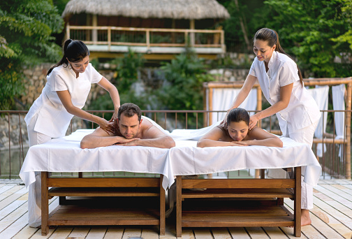 Happy couple getting a back massage outdoors at the spa by two beautiful masseuses - lifestyle concepts