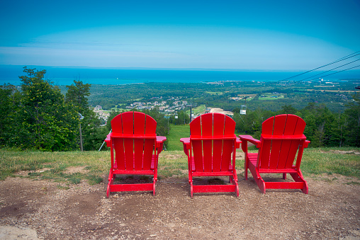 View of 3 red muskoka chairs at Blue Mountain resort and village during the summer in Collingwood, Ontario