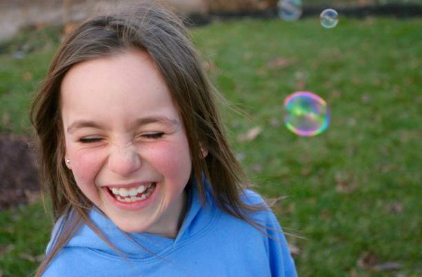 Young girl laughs as bubbles float around her face stock photo