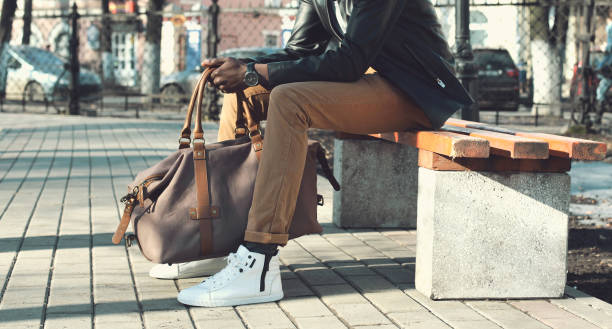 Fashion elegant african man with bag sits on the bench in the park close up stock photo