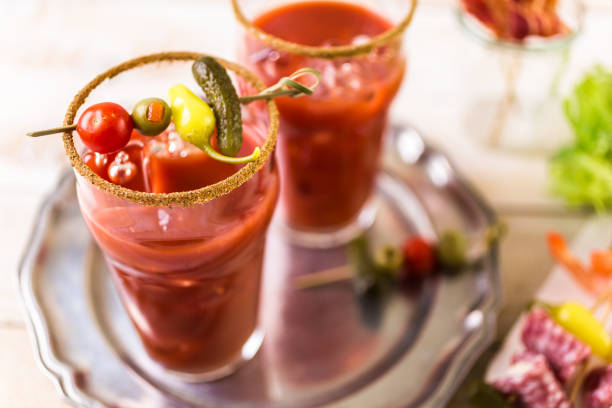 A fancy bloody mary cocktail sits on a wooden table outdoors.