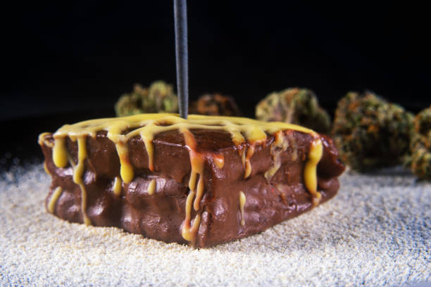 Chocolate pot brownie with cacao beans and marijuana buds - served on a white plate Macro detail of chocolate pot brownie with cacao beans and marijuana buds - served on a white plate bud candy stock pictures, royalty-free photos & images