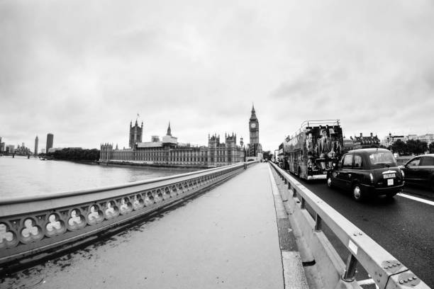 Londre, UK – August 21, 2017: View of the River Thames in London, in the background Westmister is observed, the bridge is in point of flight. On the bridge is the classic red passenger truck and the london taxi. You can also see buildings from the background of the scene. Cloudy summer afternoon, taken with a fisheye. The image is in black and white.
