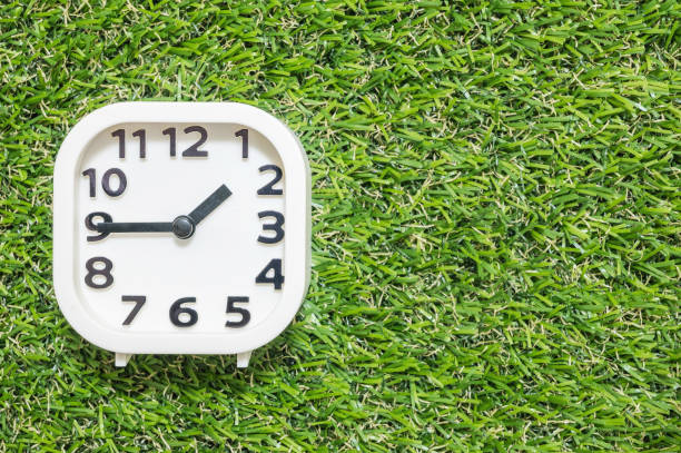 istock Closeup white clock for decorate show a quarter to two o'clock or 1:45 p.m. on green artificial grass floor textured background with copy space 855291010