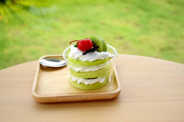 Three layer of green sofe cake with whipping cream and toping with chocolate cherry  and kiwi on wooden table and green grass hedge or bush background Three layer of green sofe cake with whipping cream and toping with chocolate cherry  and kiwi on wooden table and green grass hedge or bush background sofe stock pictures, royalty-free photos & images