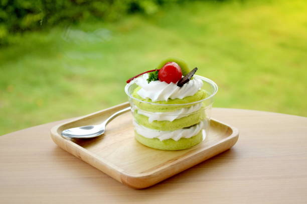 Three layer of green sofe cake with whipping cream and toping with chocolate cherry  and kiwi on wooden table and green grass hedge or bush background Three layer of green sofe cake with whipping cream and toping with chocolate cherry  and kiwi on wooden table and green grass hedge or bush background sofe stock pictures, royalty-free photos & images