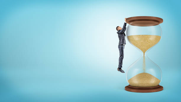 istock A tiny businessman hangs on his hangs from a large hourglasses wooden edge. 855313050