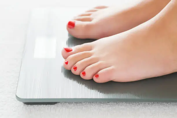 Photo of Woman with barefoot standing on the scales. Cares about a body. Weight loss concept.