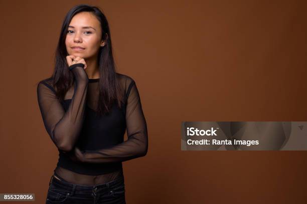 Studio Shot Of Young Asian Woman Wearing Black Long Sleeved Shirt With Sheer Fabric Against Colored Background Stock Photo - Download Image Now