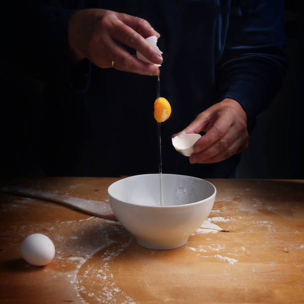 istock older women hands breaking an egg with falling egg yolk over a bowl, wooden kitchen board, dark background with copy space 855333890
