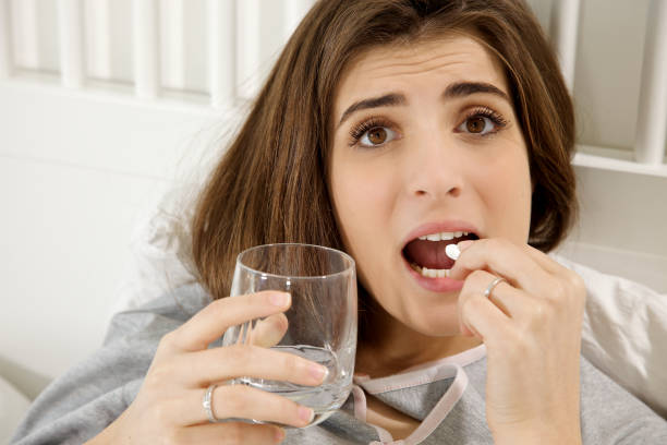 istock Sad sick woman in bed putting pill in mouth 855336502