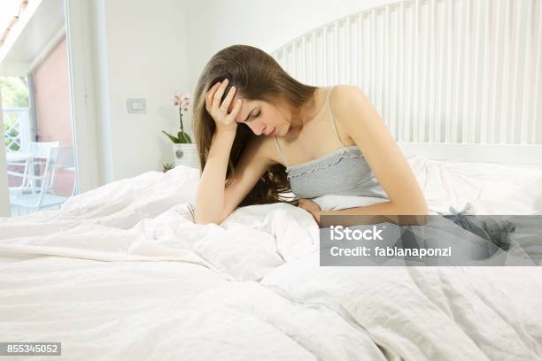 Beautiful Woman With Long Hair Sitting In Bed Sick With Strong Stomach Ache Stock Photo - Download Image Now