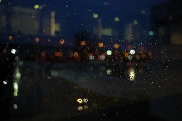 Bokeh nightlight view from raindrop window glass in dark night