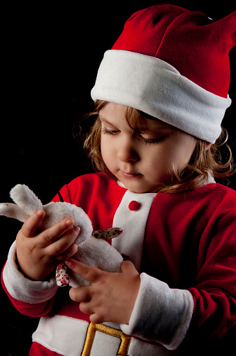 Little caucasian girl dressed as Santa Claus. Close-up portrait on black background