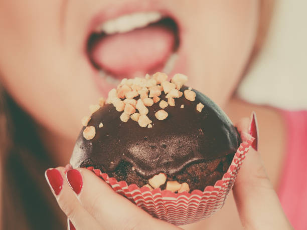 Diet, sweets, food concept. Woman holding delicious chocolate cupcake with peanut frosting, having wide open mouth about to take bite