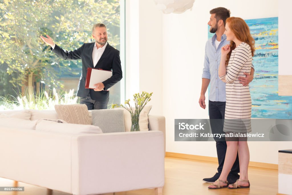 Agent showing home interior Real estate agent showing home interior for sale to young couple Real Estate Agent Stock Photo