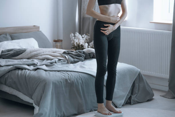Overly thin girl on a scale Overly thin teenage girl standing on a scale pulling her stomach in photos of anorexia pictures stock pictures, royalty-free photos & images